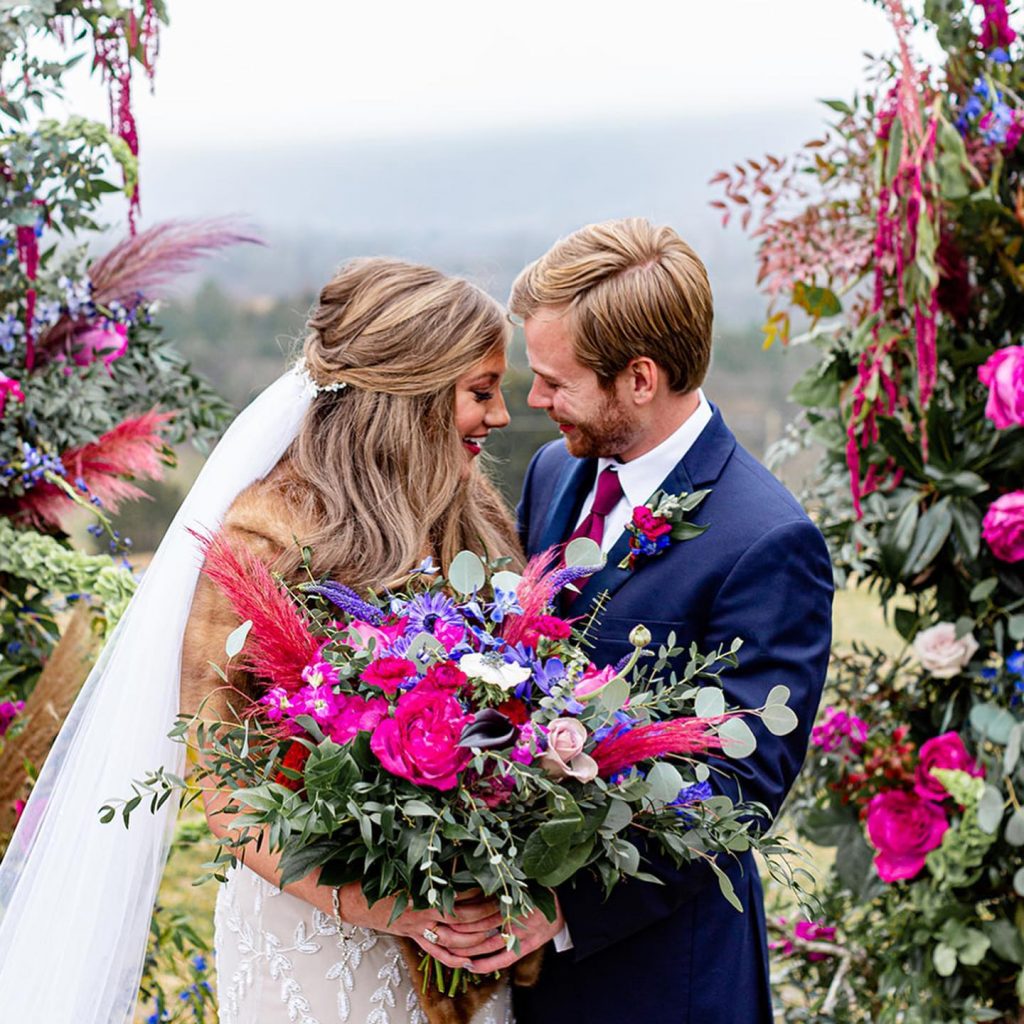 Bride and groom looking at each other surrounded by dark blue and fuchsia flowers.