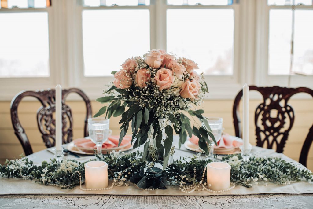 Table setting from an elopement with greenery, candles, pink roses, and pearls.