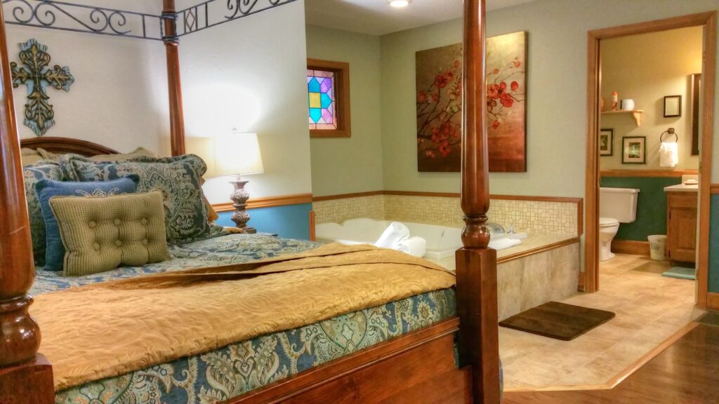 A wide view of a room with a four-poster bed, a stained glass window, and a bathroom with a tub and toilet.