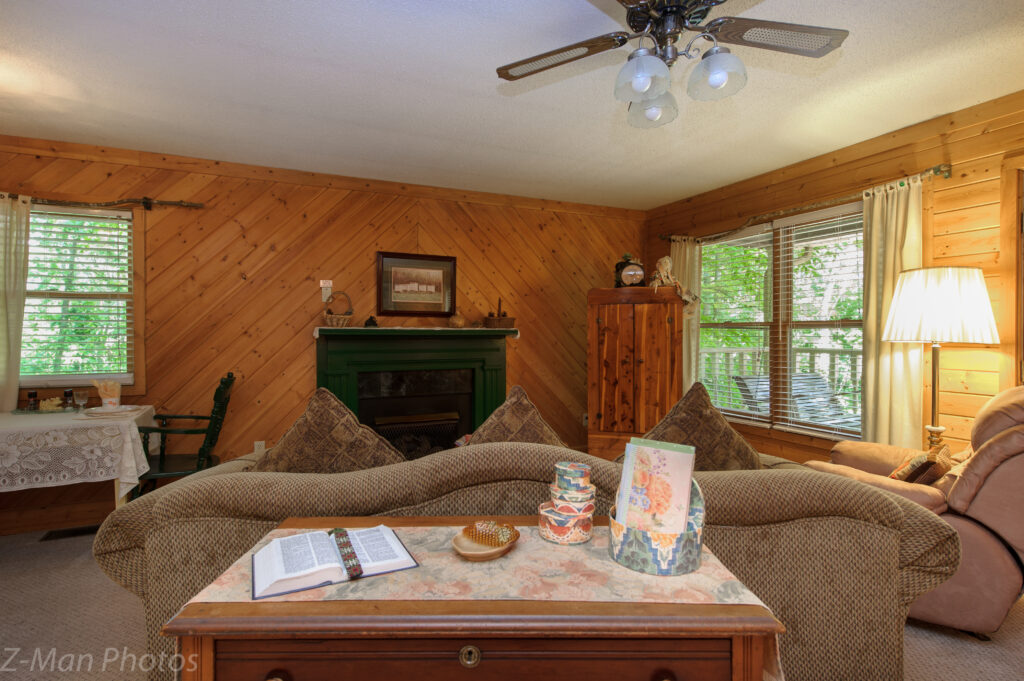 A cozy living room with wood paneling, a fireplace, and a ceiling fan.