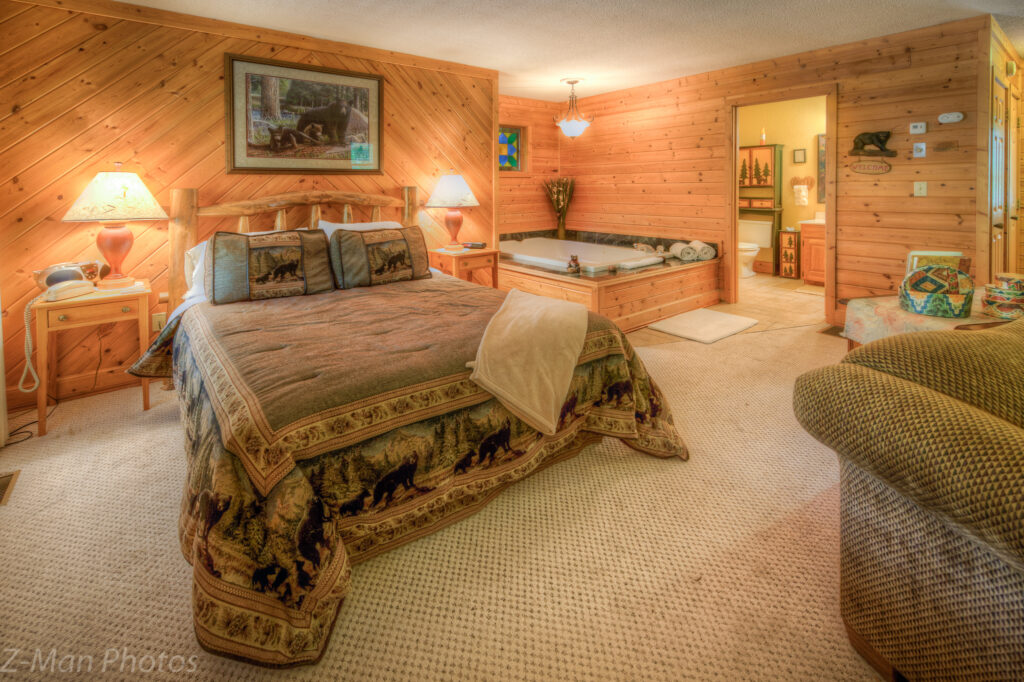 A wide-angle view of a wood-paneled suite with a king-sized bed, a jacuzzi tub, and a sofa.