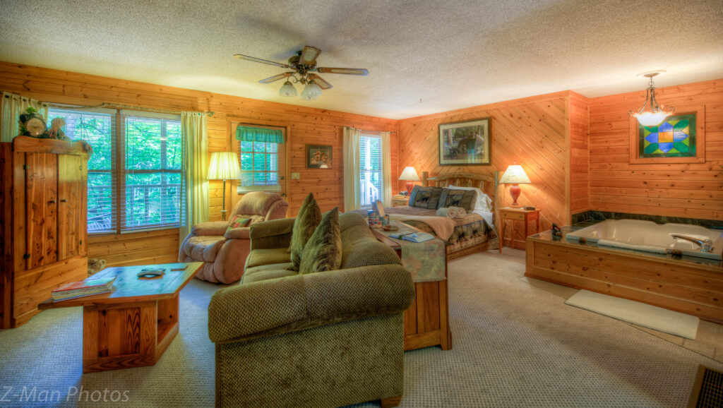 A wide view of a wood-paneled suite with a sofa, coffee table, bed, and jacuzzi tub.