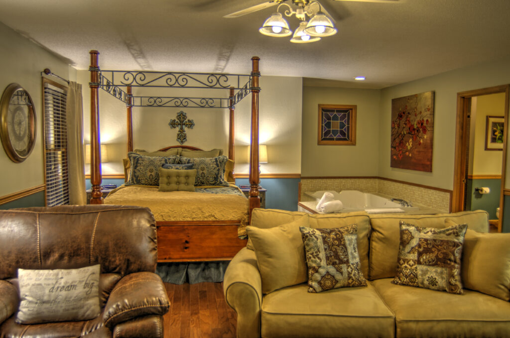A wide view of a suite with a king-size bed, jacuzzi, sofa, and armchair.