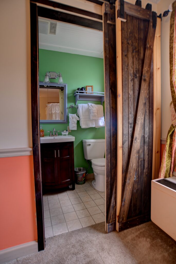 A bathroom with a sliding barn door, green wall, dark wood vanity, and white toilet.