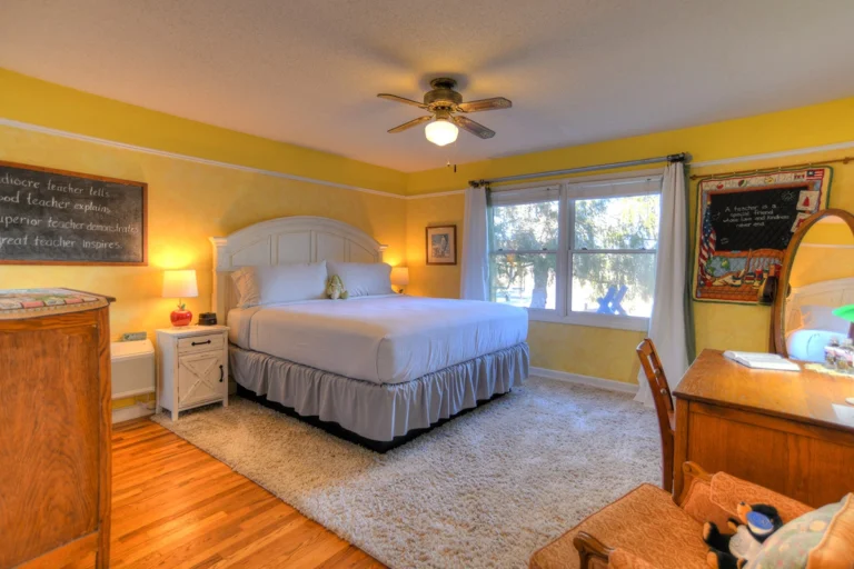 A wide-angle view of a bedroom with a bed, desk, and window.