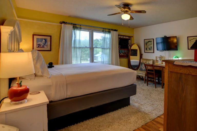 A wide view of a guest room with a bed, desk, TV, and window.